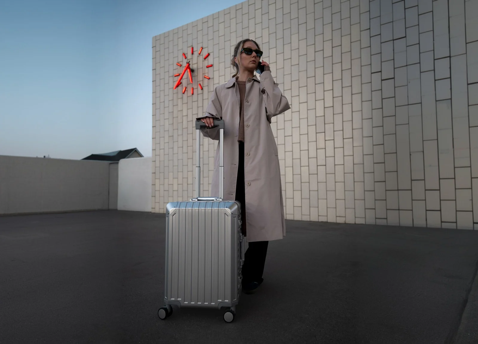 Traveler in a trench coat standing with silver luggage