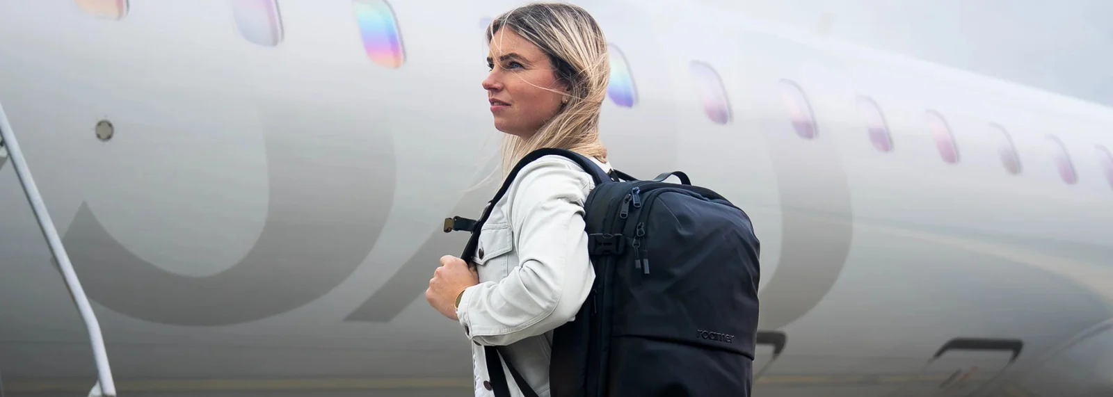 Traveler wearing a dark backpack beside an airplane